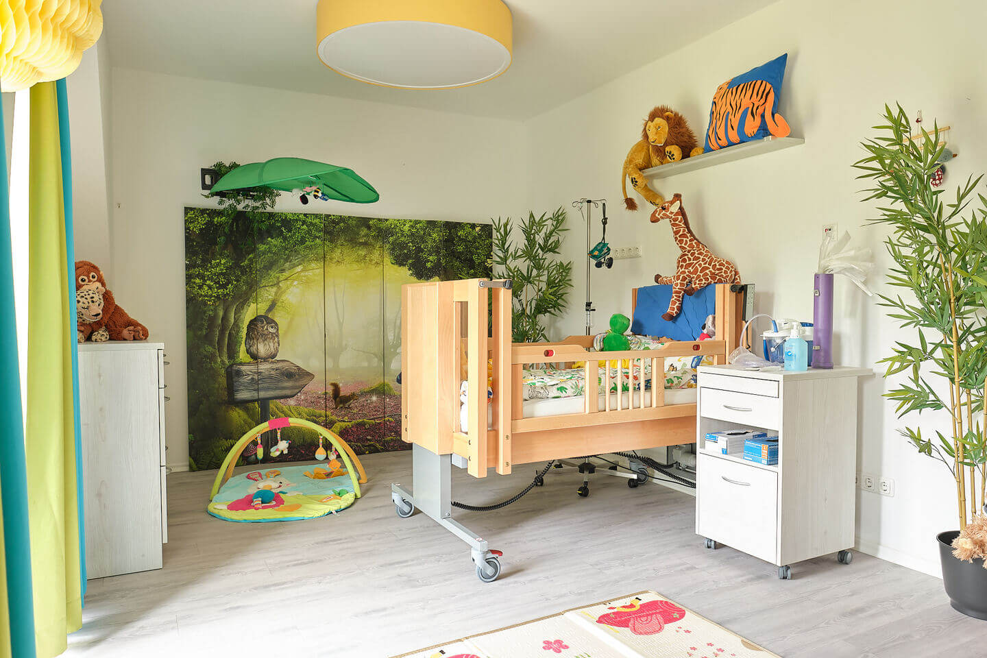 Liebevoll eingerichtetes Kinderpflegezimmer mit Spezialbett und Waldwandbild